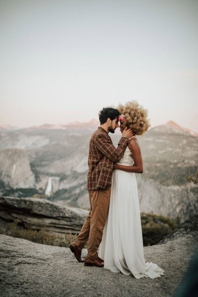 Elopement couple posing on the edge of a rocky overlook with Half Dome glowing at sunset