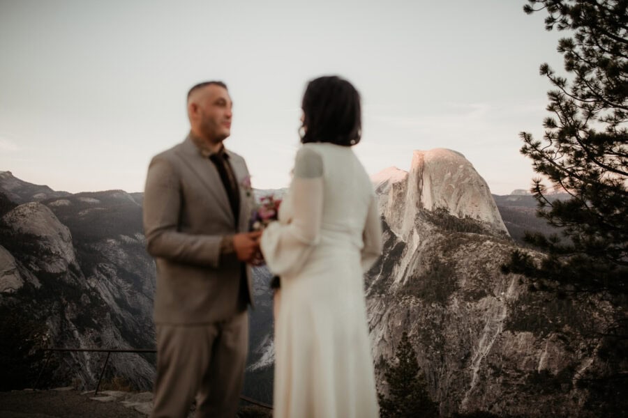 Elopement couple posing on the edge of a rocky overlook with Half Dome glowing at sunset