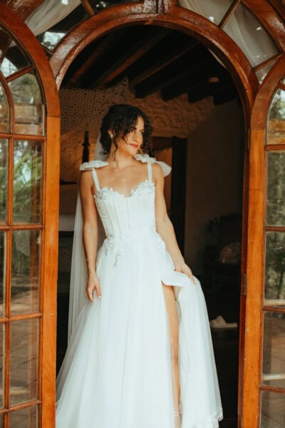 Bride standing in rustic wooden door frame in white wedding dress