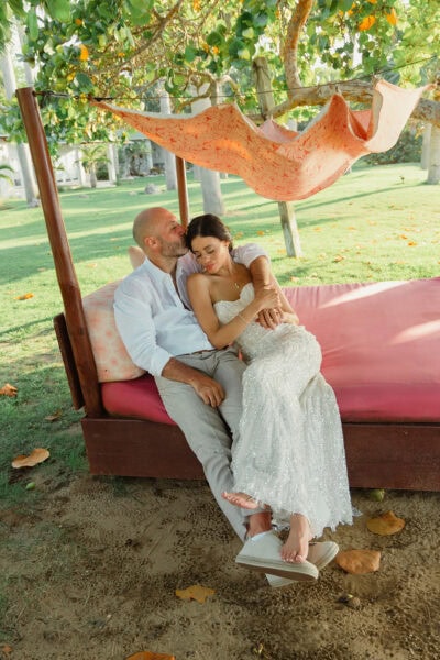 Man and Woman sitting and cuddling together after getting married, with her in a white dress looking lovingly at him