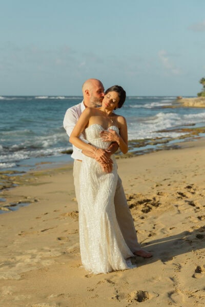 Man and Woman standing together on the beach after getting married, with her in a white dress looking lovingly at him