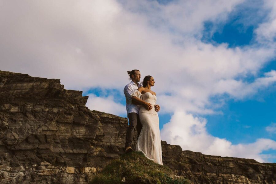 Couple eloping on cliffs at sunset in Ireland against blue skies